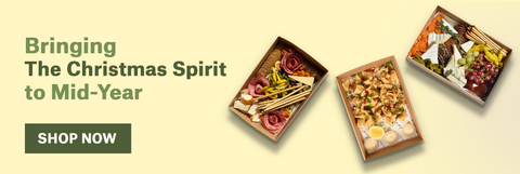 Three gift boxes with Christmas-themed items on a beige background, with text 'Bringing The Christmas Spirit to Mid-Year' and 'Shop Now' button.